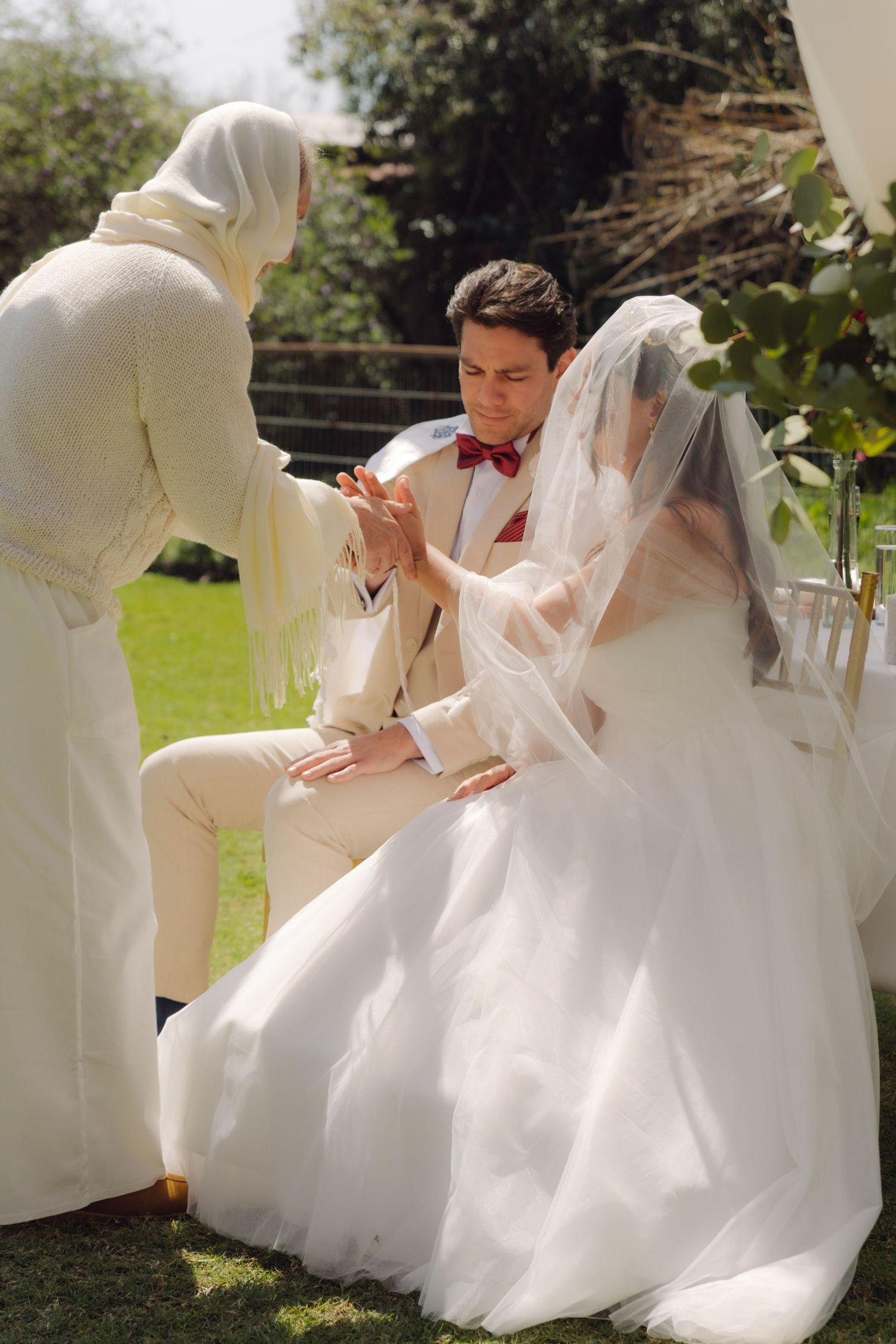 Officiant performs blessing ritual with bride and groom during outdoor Jewish wedding.