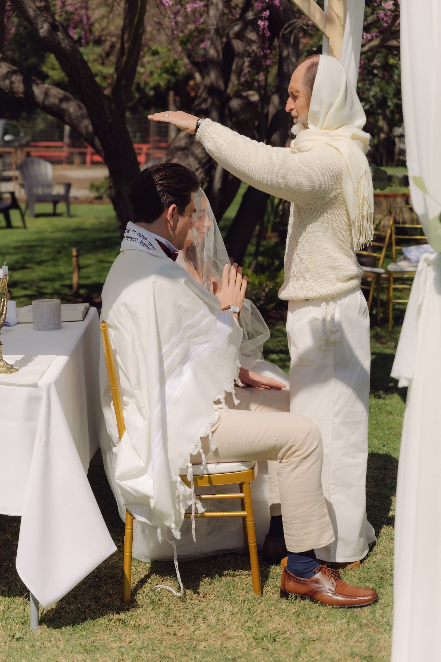 Officiant blesses groom with raised hand during intimate outdoor Jewish wedding ceremony.