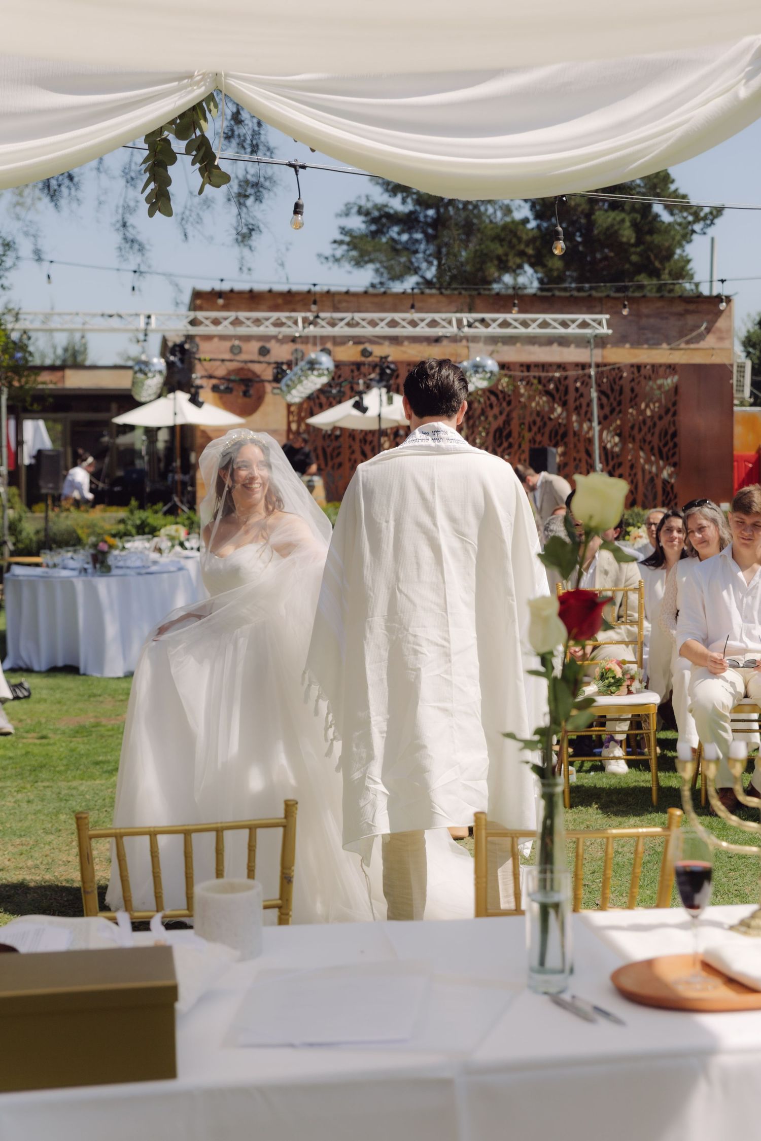Bride and groom walk together down the aisle at an elegant outdoor wedding ceremony under a white canopy.