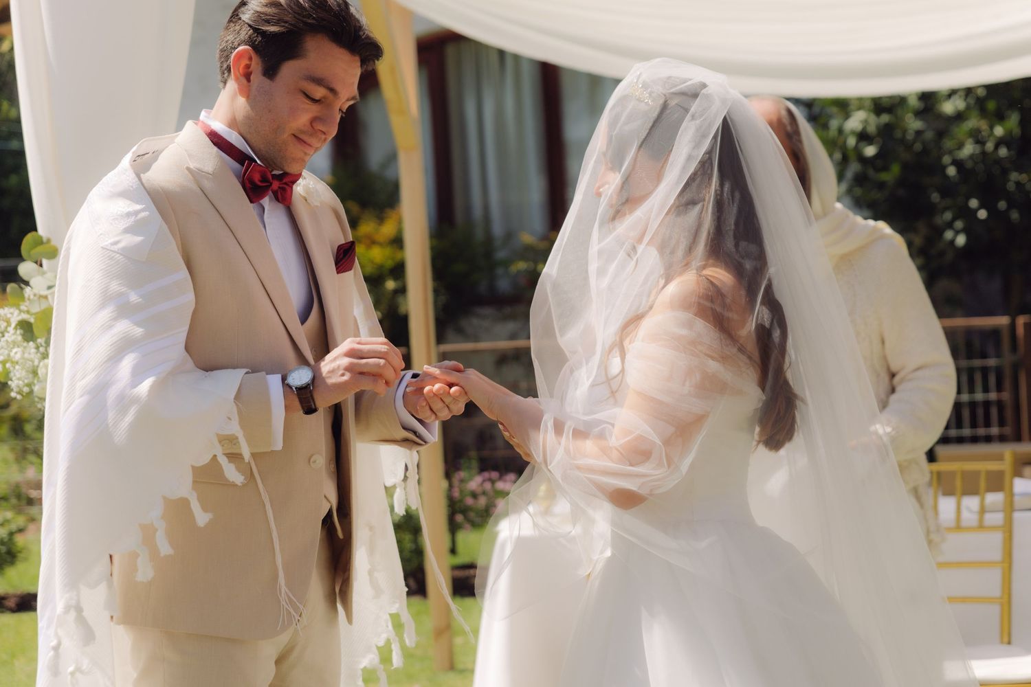 Groom places wedding ring on bride's finger during intimate outdoor Jewish wedding ceremony.