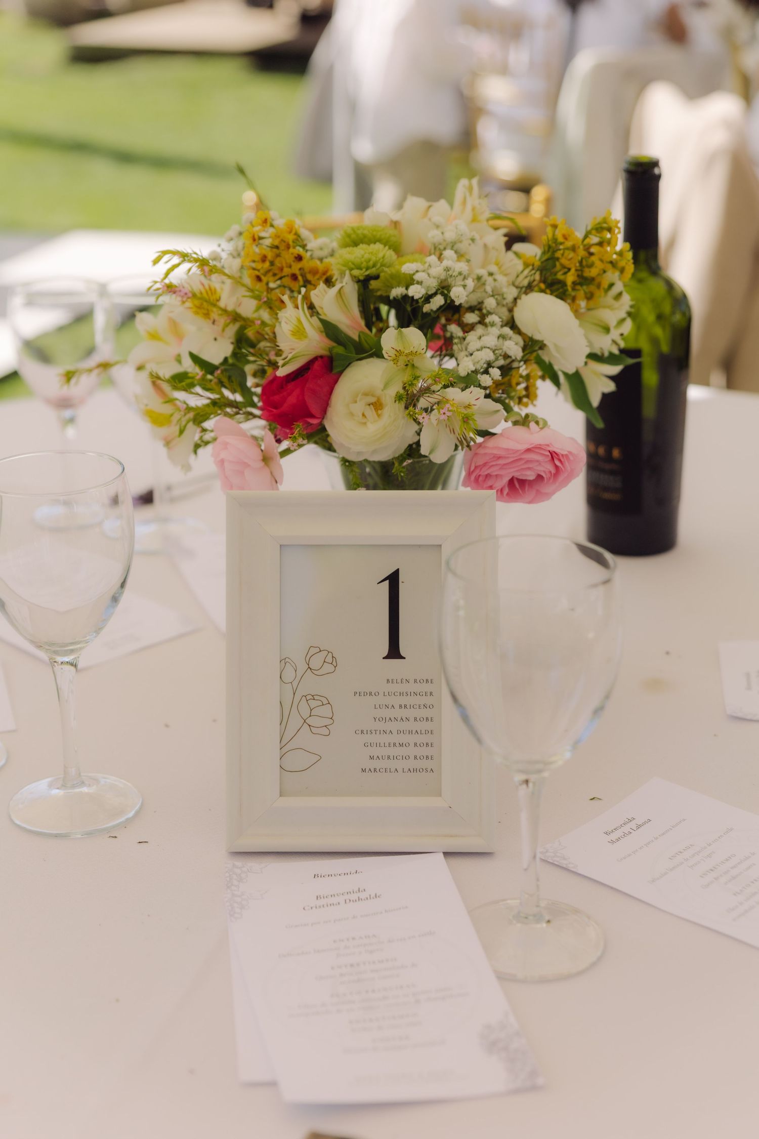Elegant wedding table centerpiece with colorful flowers, table number one, and wine glasses.