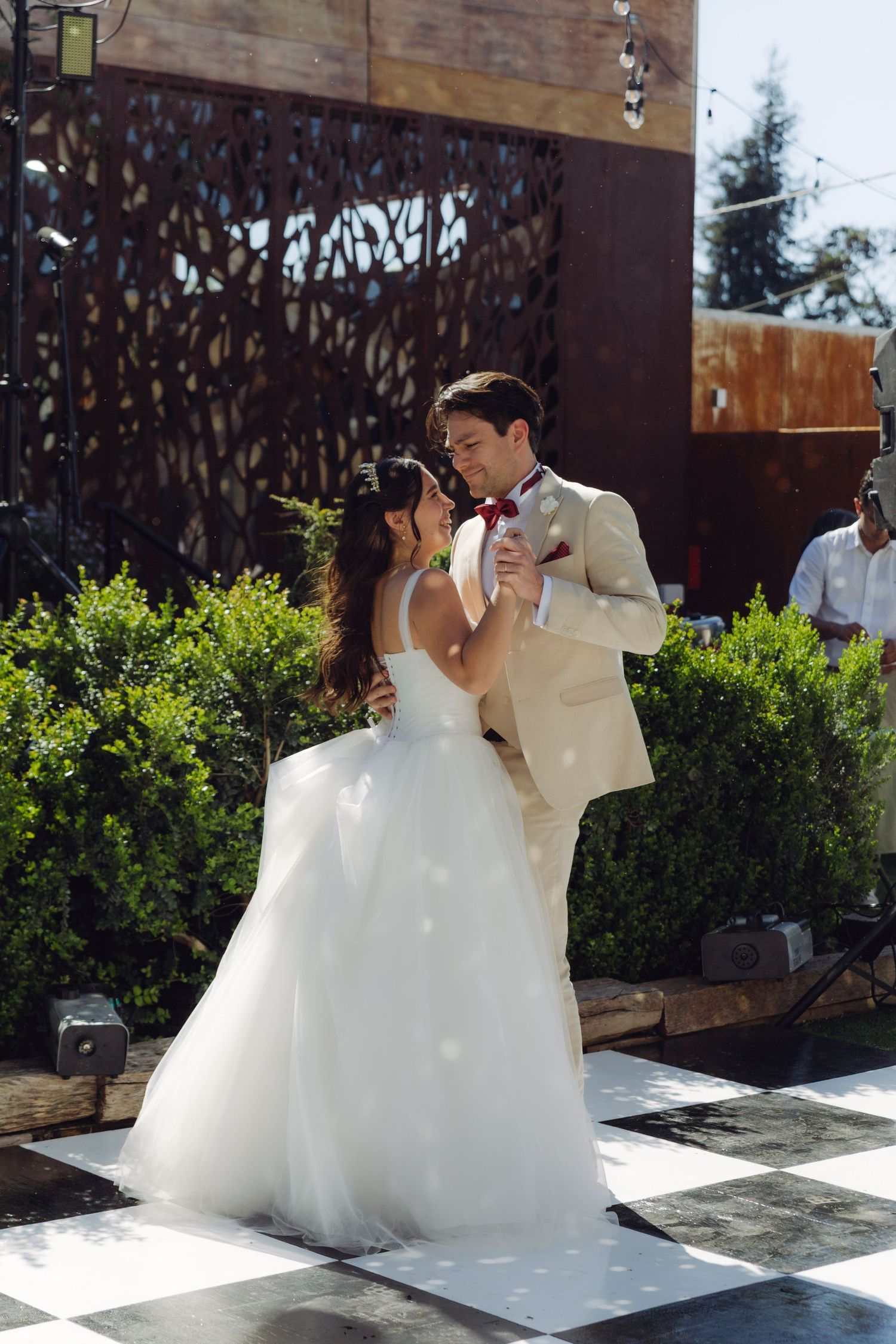 Newlyweds share an intimate first dance on a black and white checkered outdoor dance floor at their wedding.