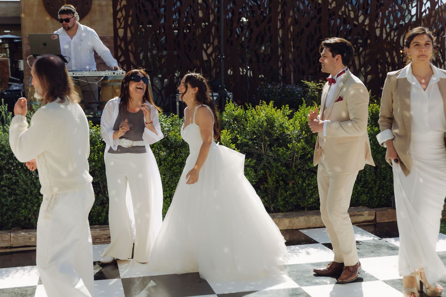 Wedding guests dressed in white dance and celebrate on an outdoor checkered dance floor during the reception.