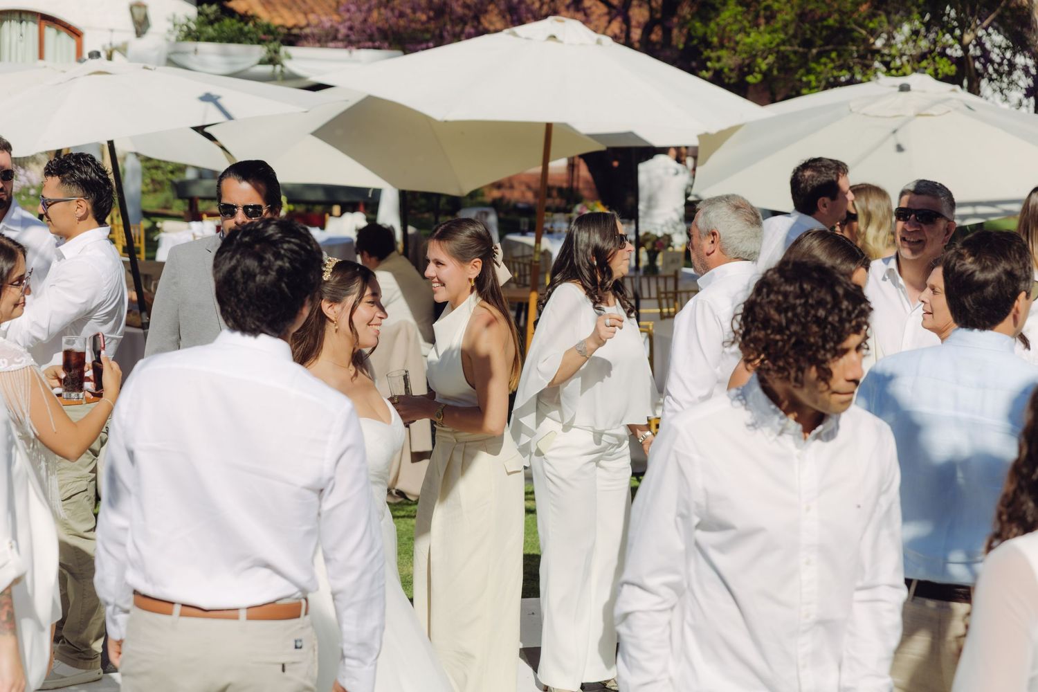 Elegantly dressed wedding guests in white socialize and enjoy the outdoor daytime wedding reception.