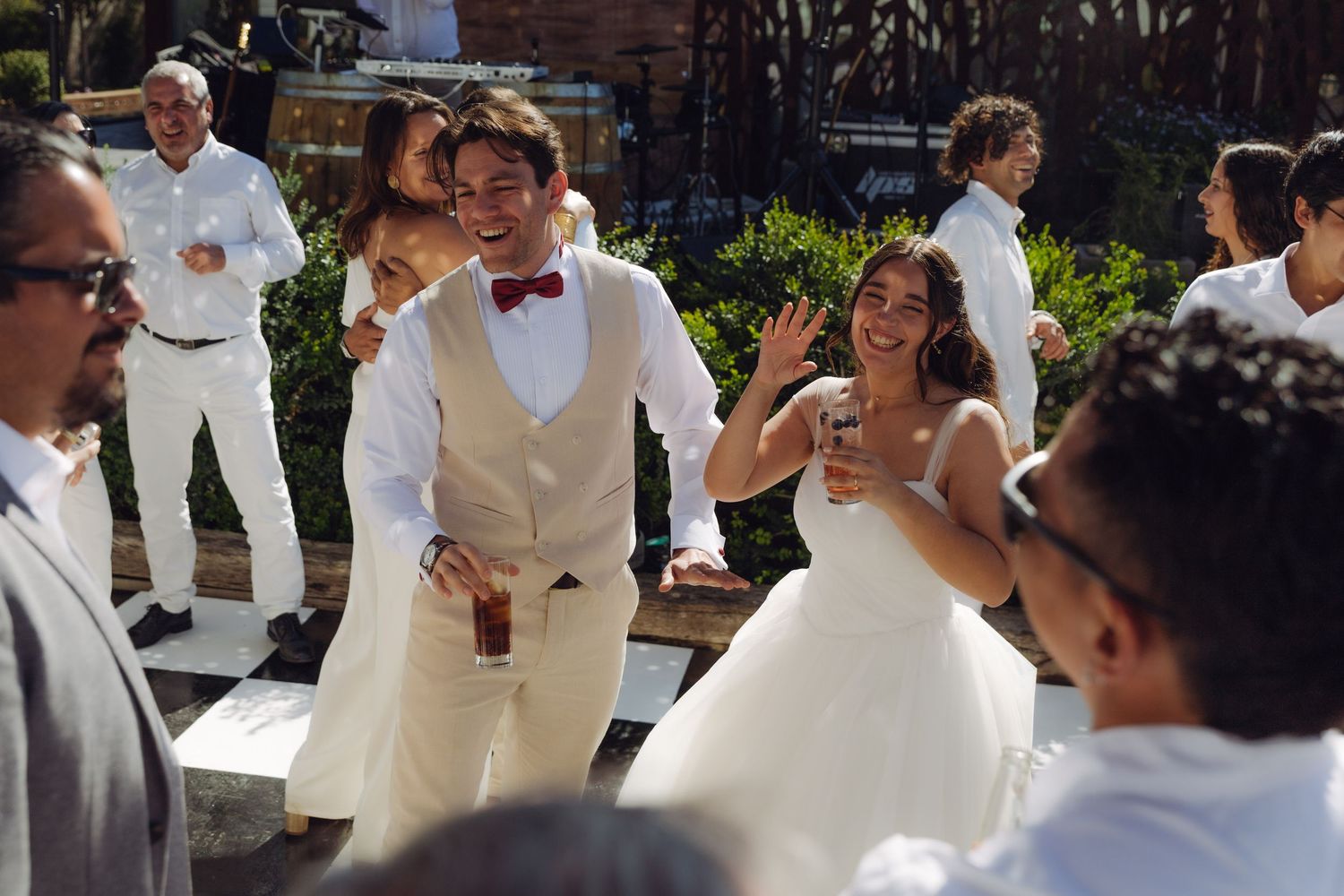 Groom in white vest with red bow tie dancing with bride in ball gown at outdoor wedding.