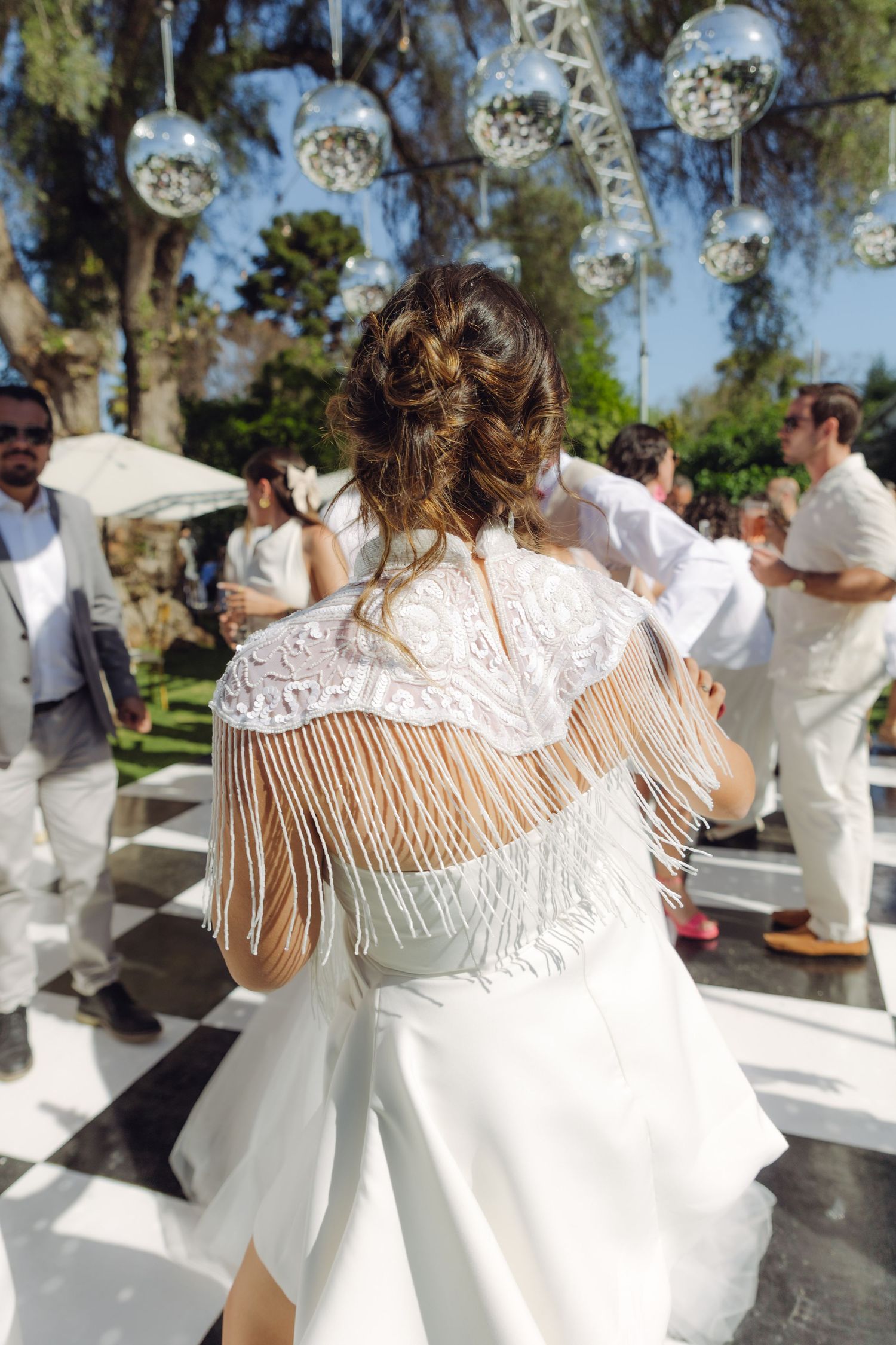 Back view of woman in white fringed lace shawl dancing at outdoor wedding reception.