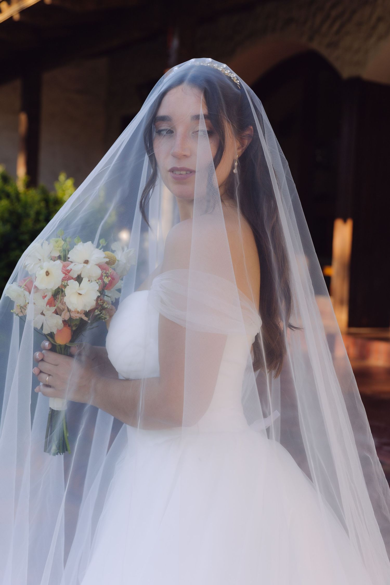 Beautiful bride wearing a white ball gown and veil holding a colorful bridal bouquet outdoors.