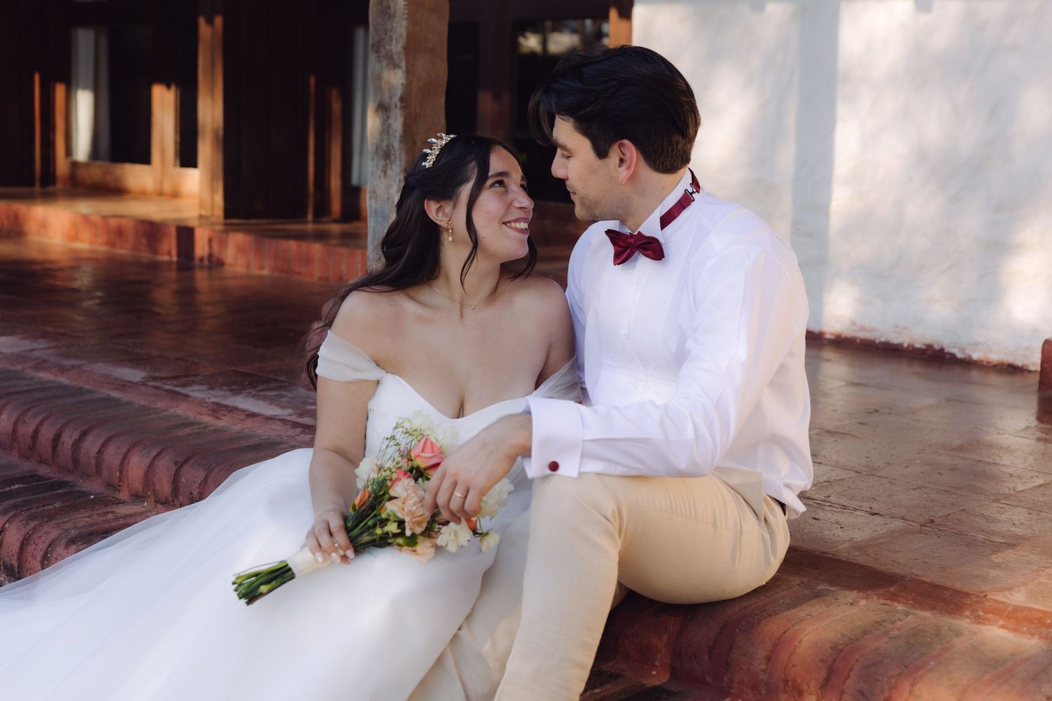 Bride and groom sitting together on steps, bride holding a pink and white bridal bouquet.