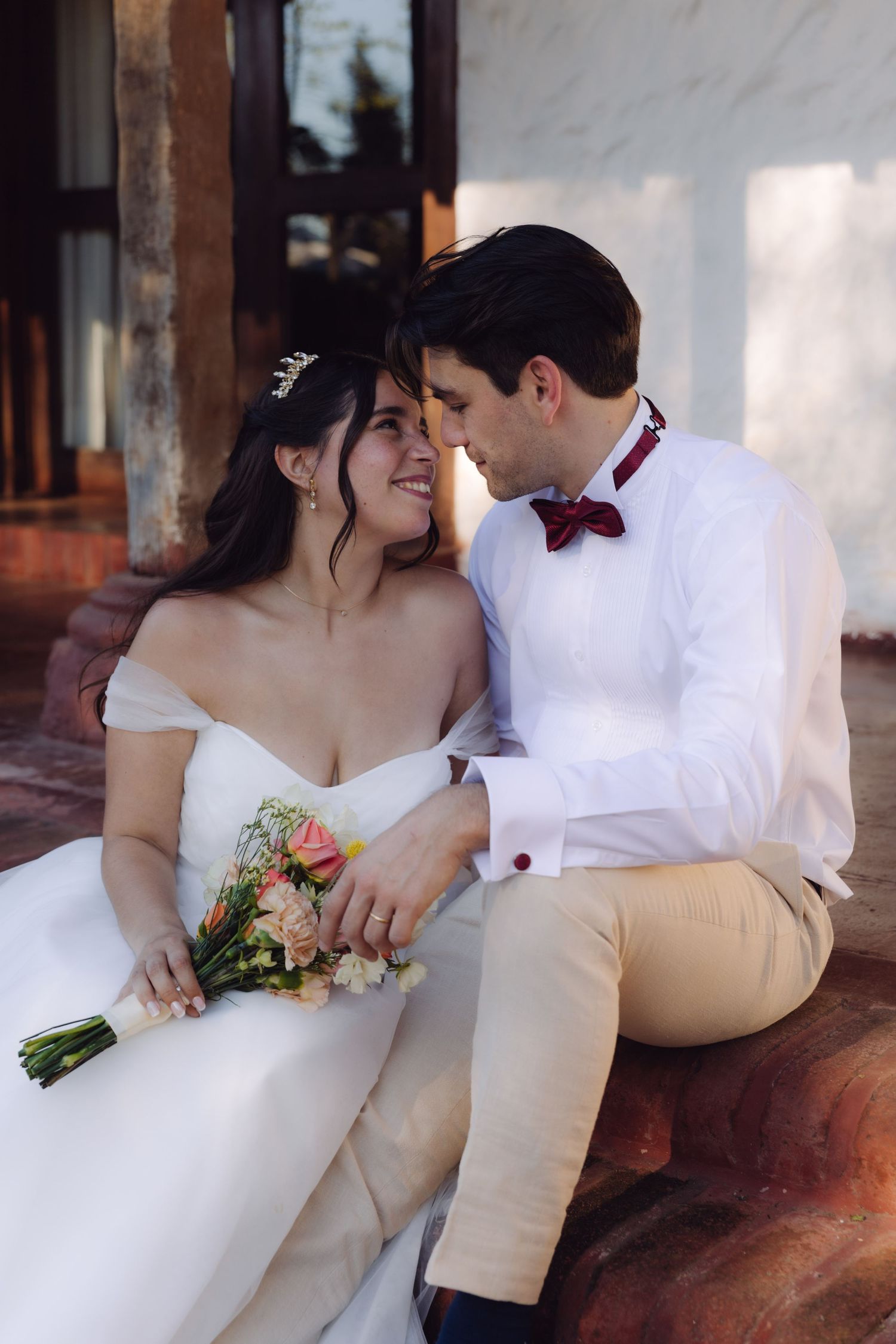 Bride and groom sitting closely together, bride holding a colorful bouquet at their wedding venue.