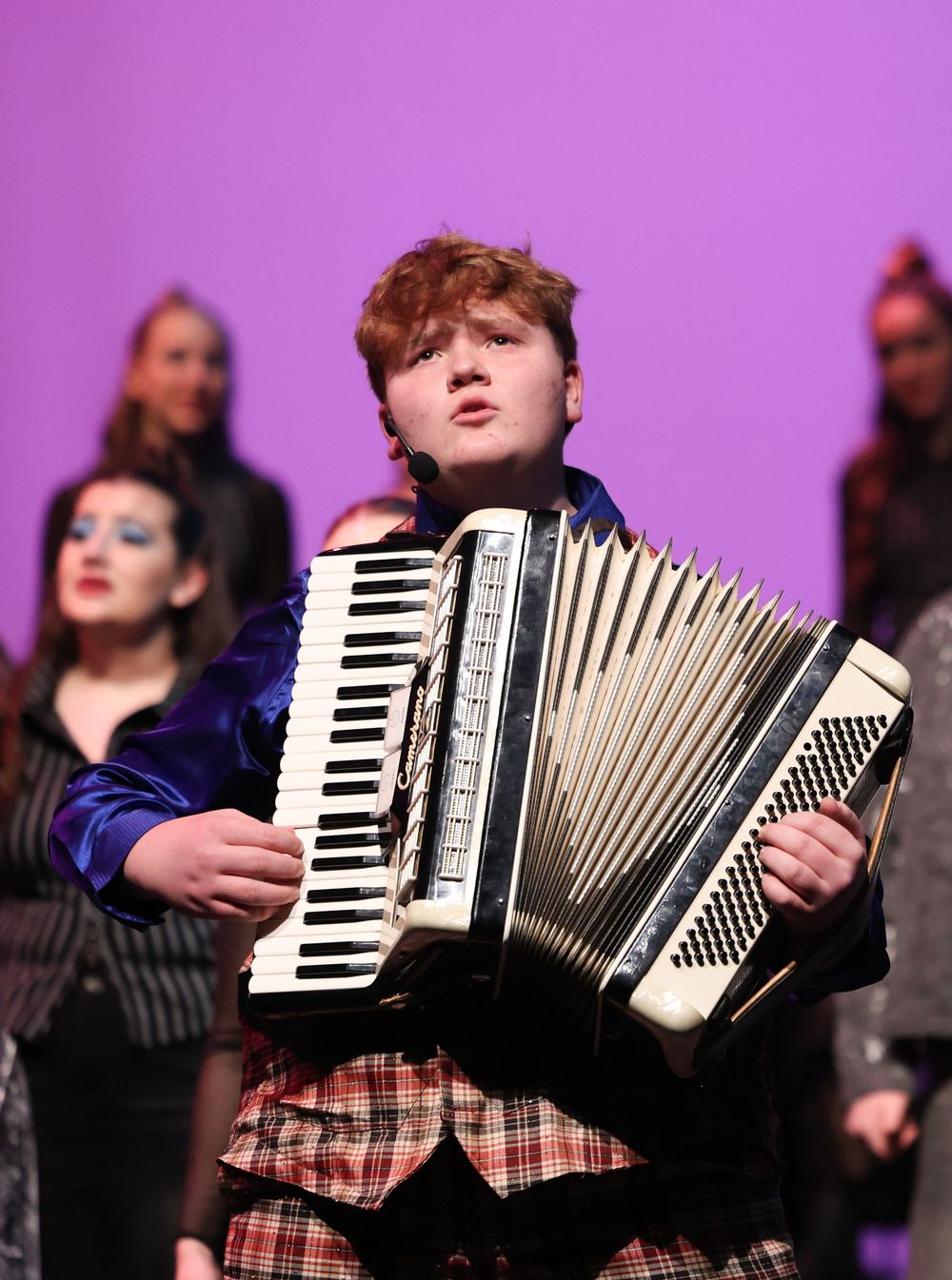 Musicians playing accordions in a performance with purple stage lighting.