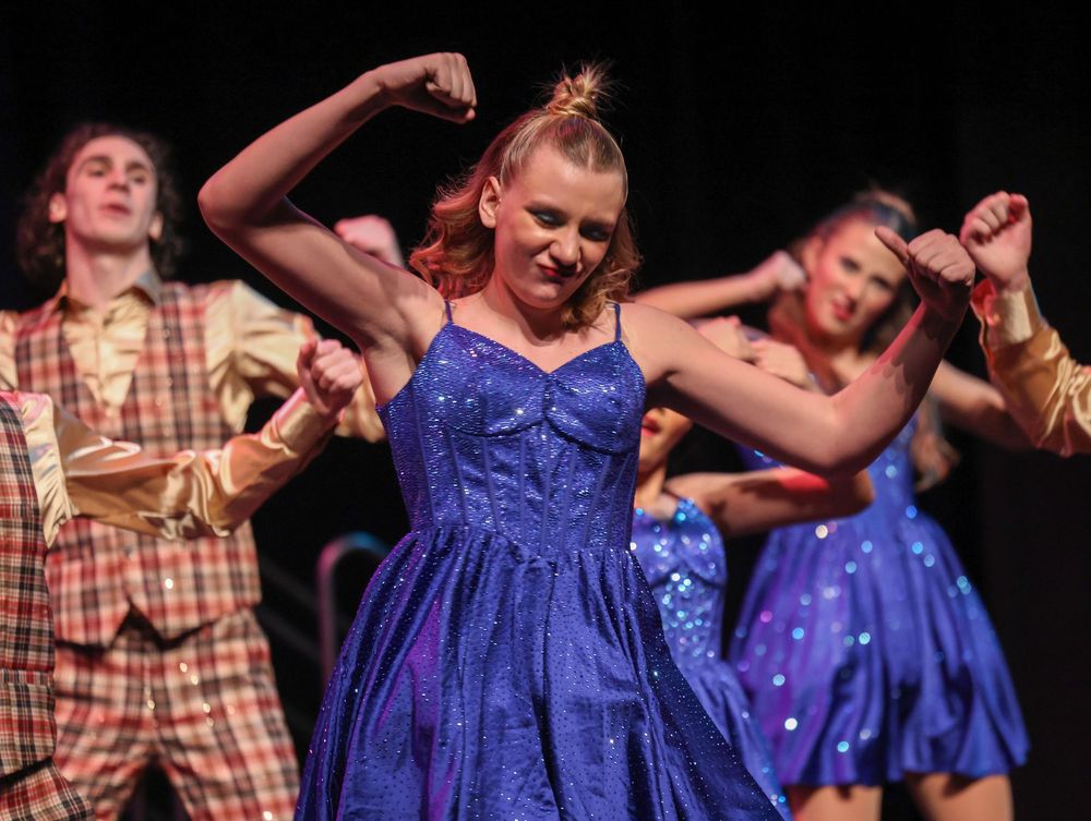 Performers in blue sparkly dresses and plaid shirts dancing on stage.