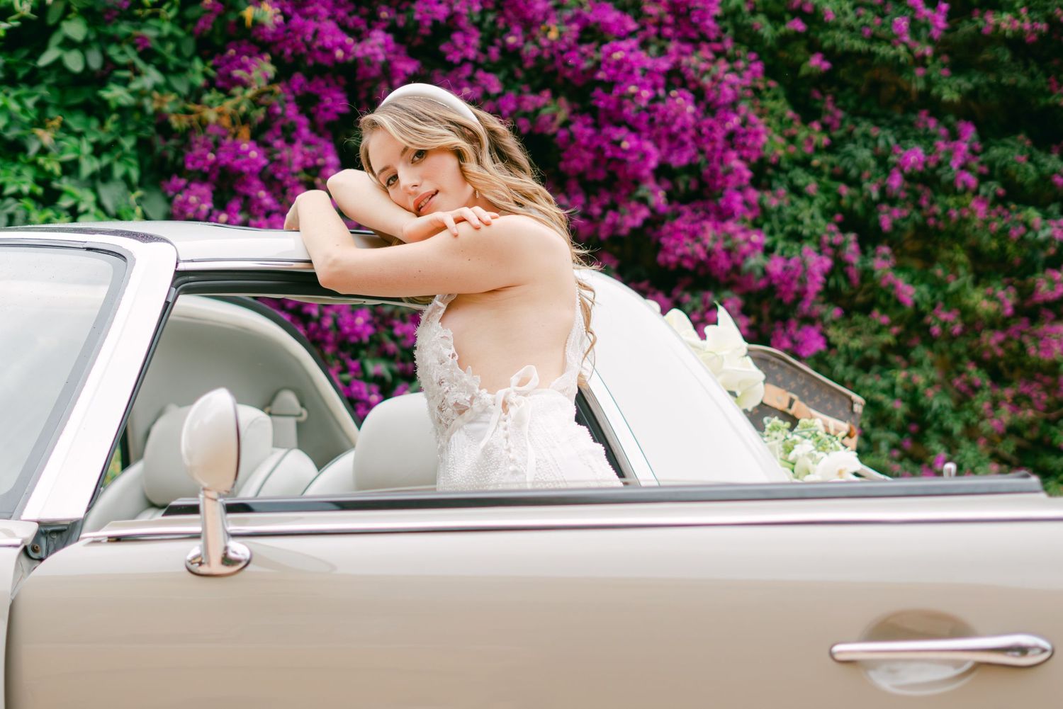 Mariée en robe blanche appuyée sur une voiture décapotable, bougainvilliers en arrière-plan, lumière de Provence.