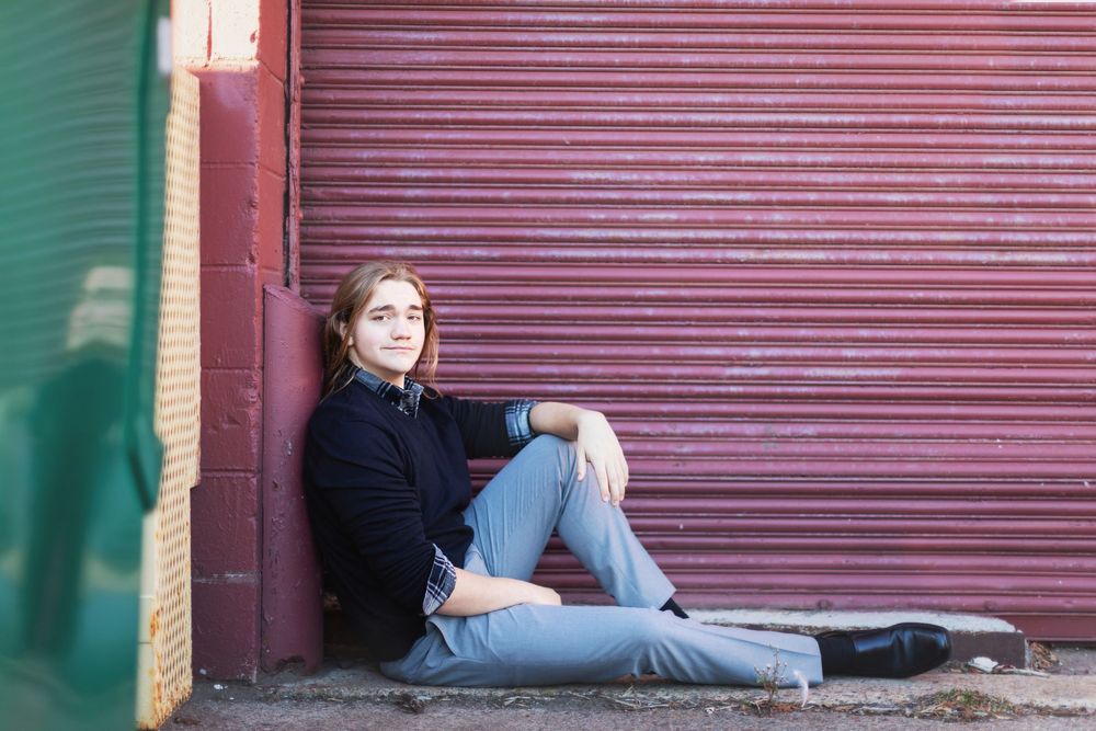 A person in casual wear lounges against a red metal shutter door with green walls on either side.
