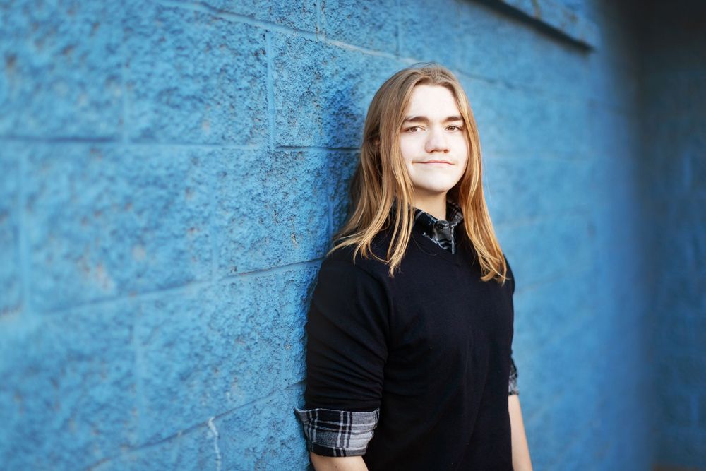 A figure in a black turtleneck sweater poses against a blue textured wall in a series of similar shots.