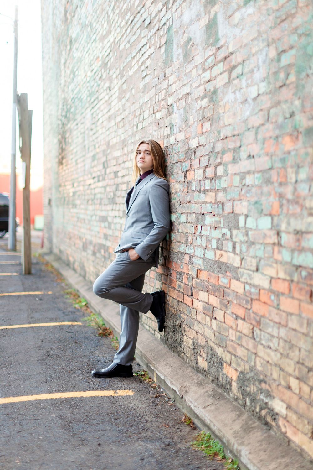 A series of poses against a brick wall showing someone wearing a gray business suit and black shoes.