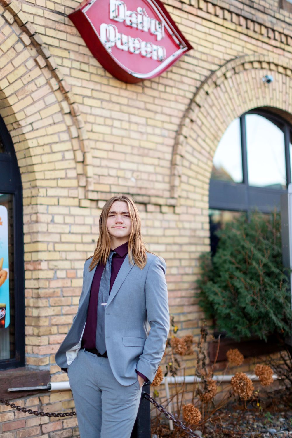 Professional wearing a gray business suit and burgundy top poses confidently against a brick building exterior.