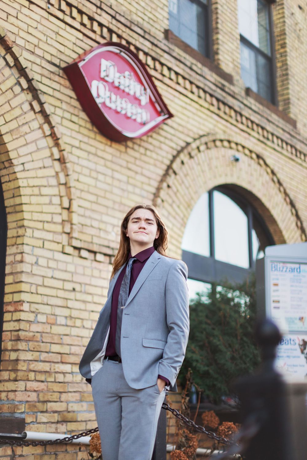 Professional wearing a gray business suit and burgundy top poses against a brick building exterior.