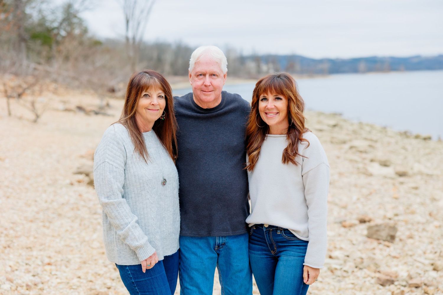 Three people pose together on a rocky beach at Tabel Rock Lake shoreline wearing casual sweaters and jeans.