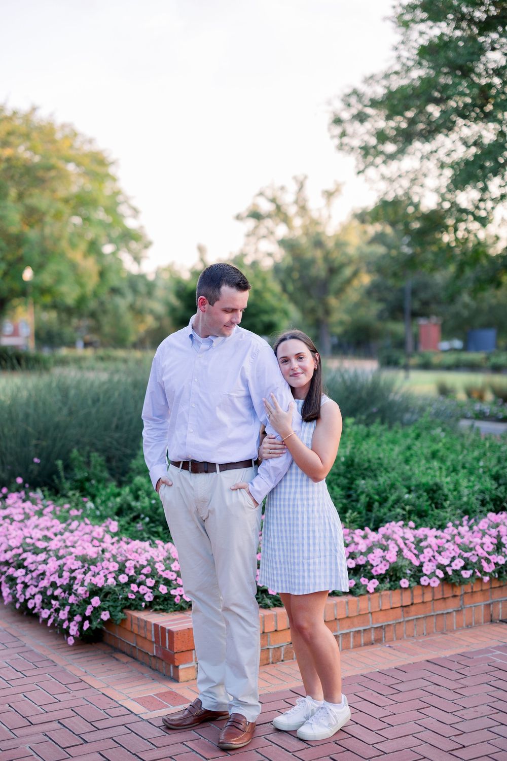 A couple shares a romantic moment together in a garden with pink flowers and brick pathways on a sunny afternoon.
