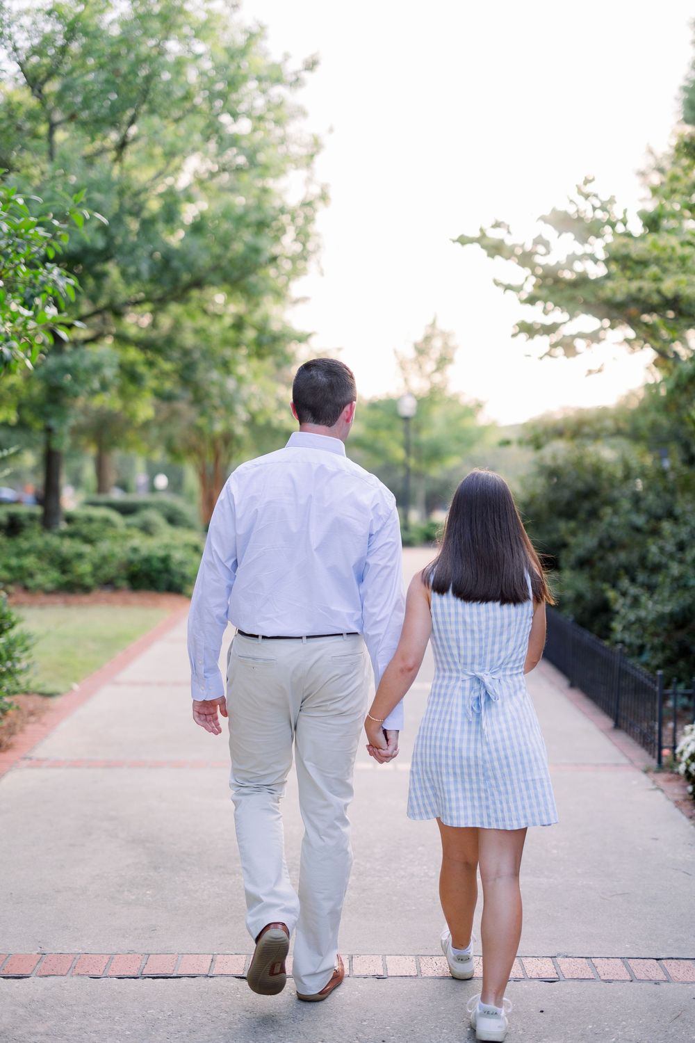 A couple walking hand in hand down a tree-lined path on a sunny day.