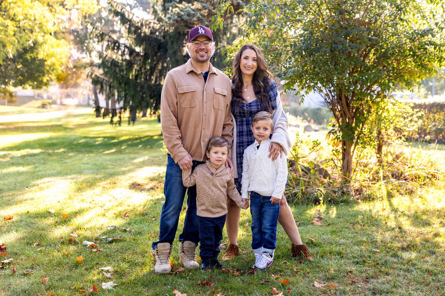 A family walks together through a sunlit park during autumn as golden leaves scatter around them.