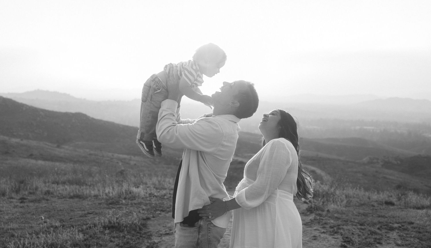A couple in white outfits shares an intimate moment together in a misty outdoor setting during an engagement photoshoot.