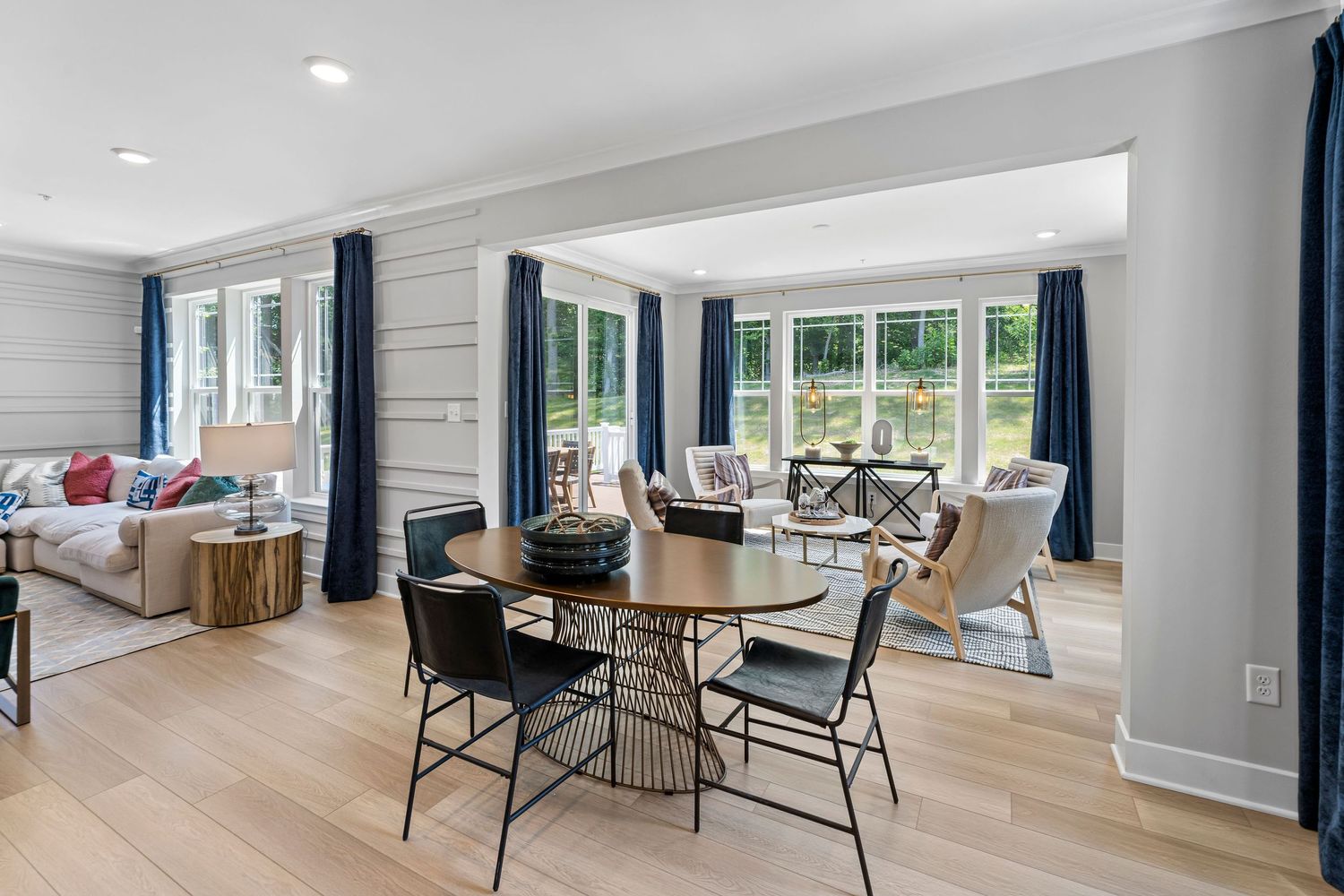 Modern open concept living room with white walls, hardwood floors, and large windows providing natural light.