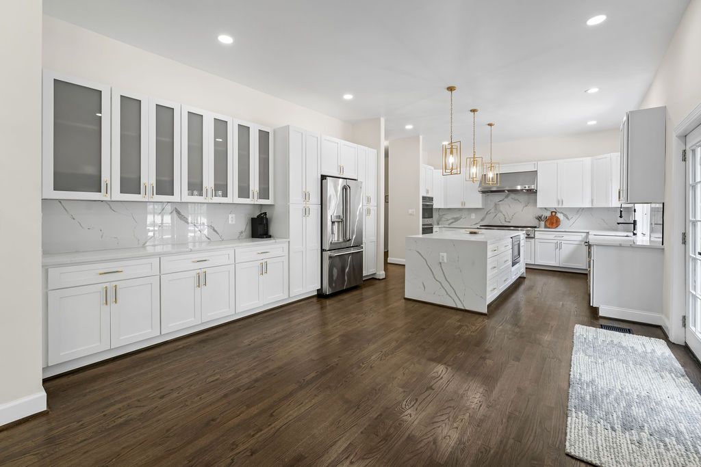 Modern white kitchen with dark hardwood floors, pendant lighting, and sleek cabinetry extending down a long open space.