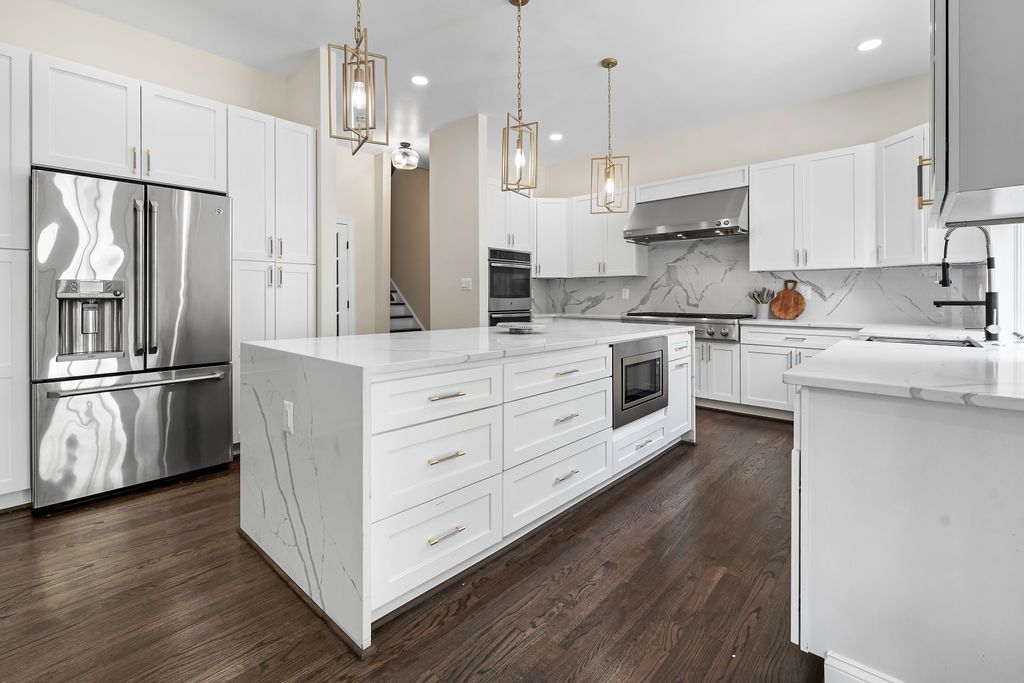 Elegant kitchen with stainless steel appliances, white cabinetry, and marble backsplash in an open floor plan.
