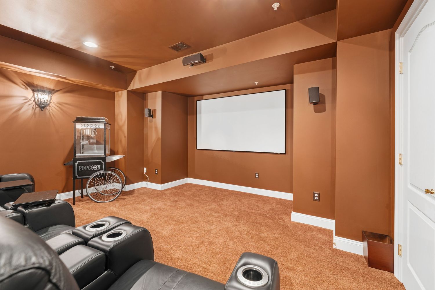 Large home theater room with black leather recliners and warm brown walls and carpet.