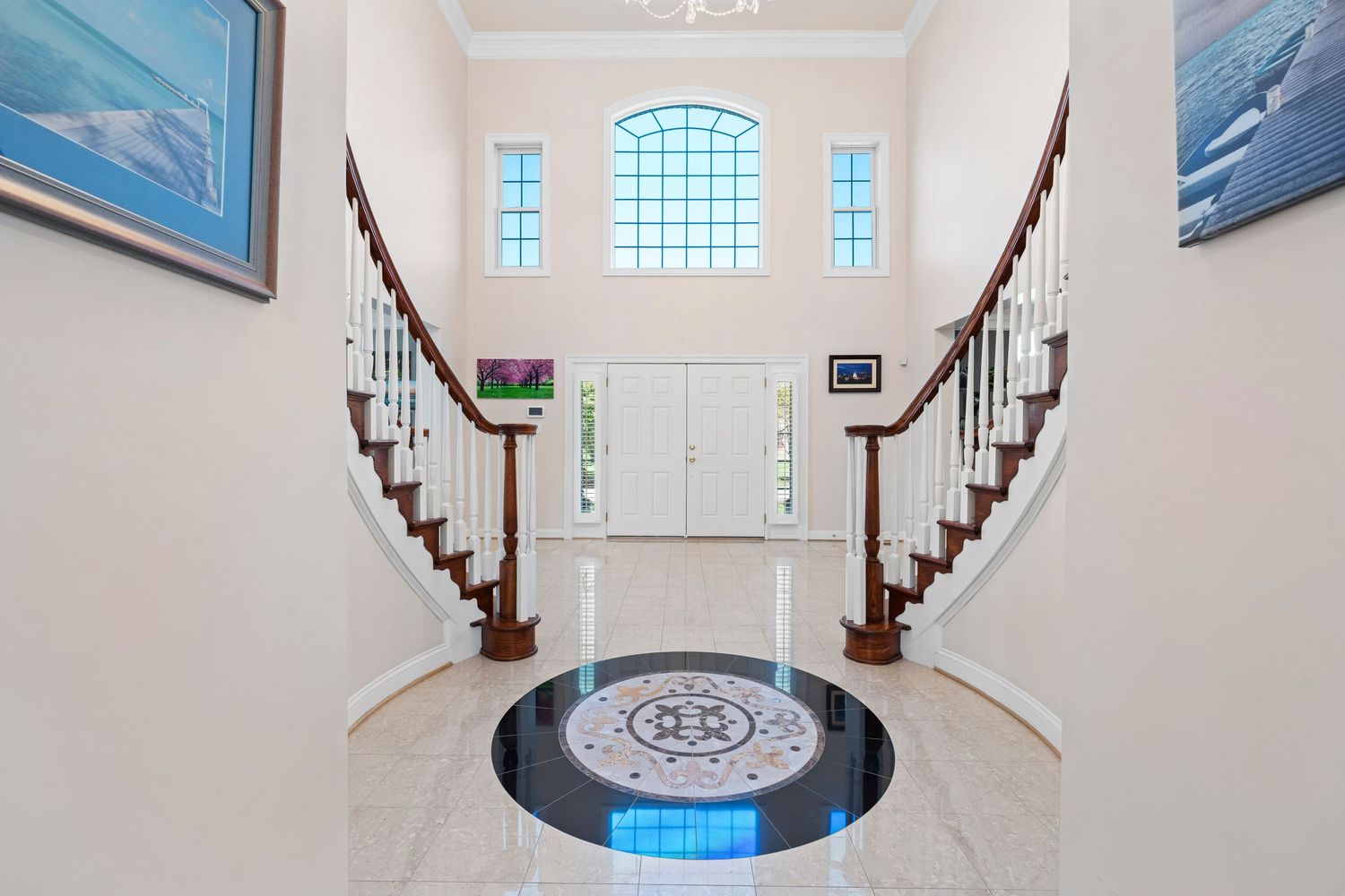 Elegant white foyer with curved staircase and crystal chandelier featuring ocean artwork.