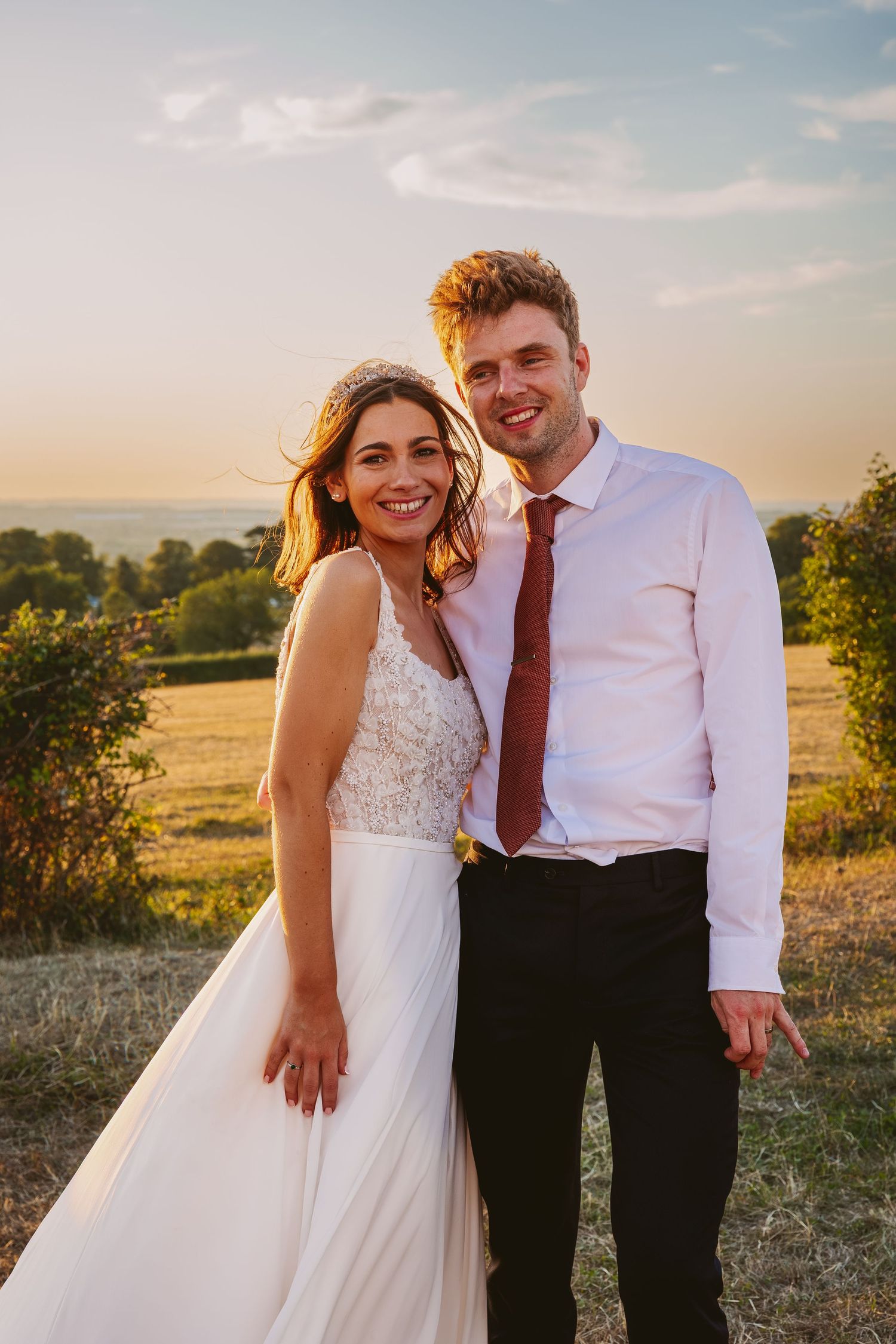 A couple shares a joyful moment in golden sunlight with rolling hills in the background.
