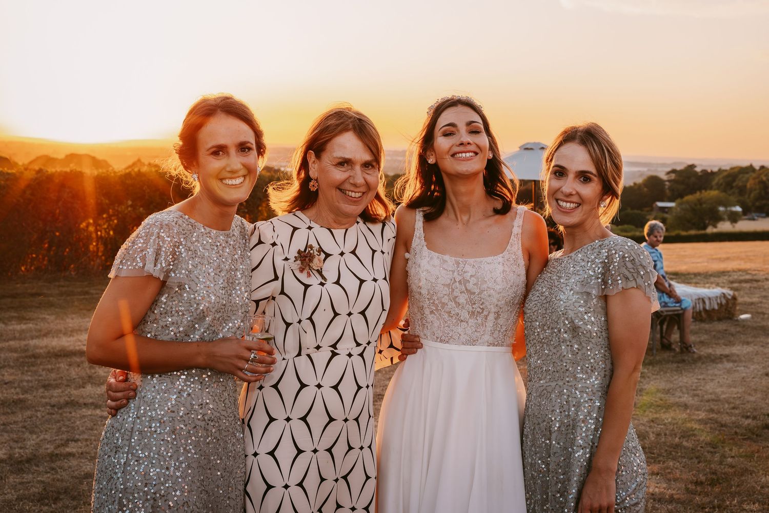 Wedding party poses together in an open field at sunset with bridesmaids in sparkly dresses.