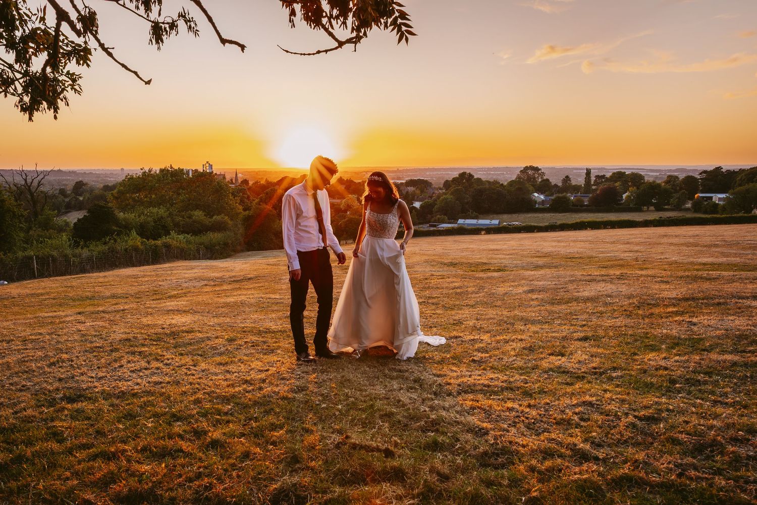 A couple walks hand in hand across a golden hillside at sunset with warm light illuminating the landscape.