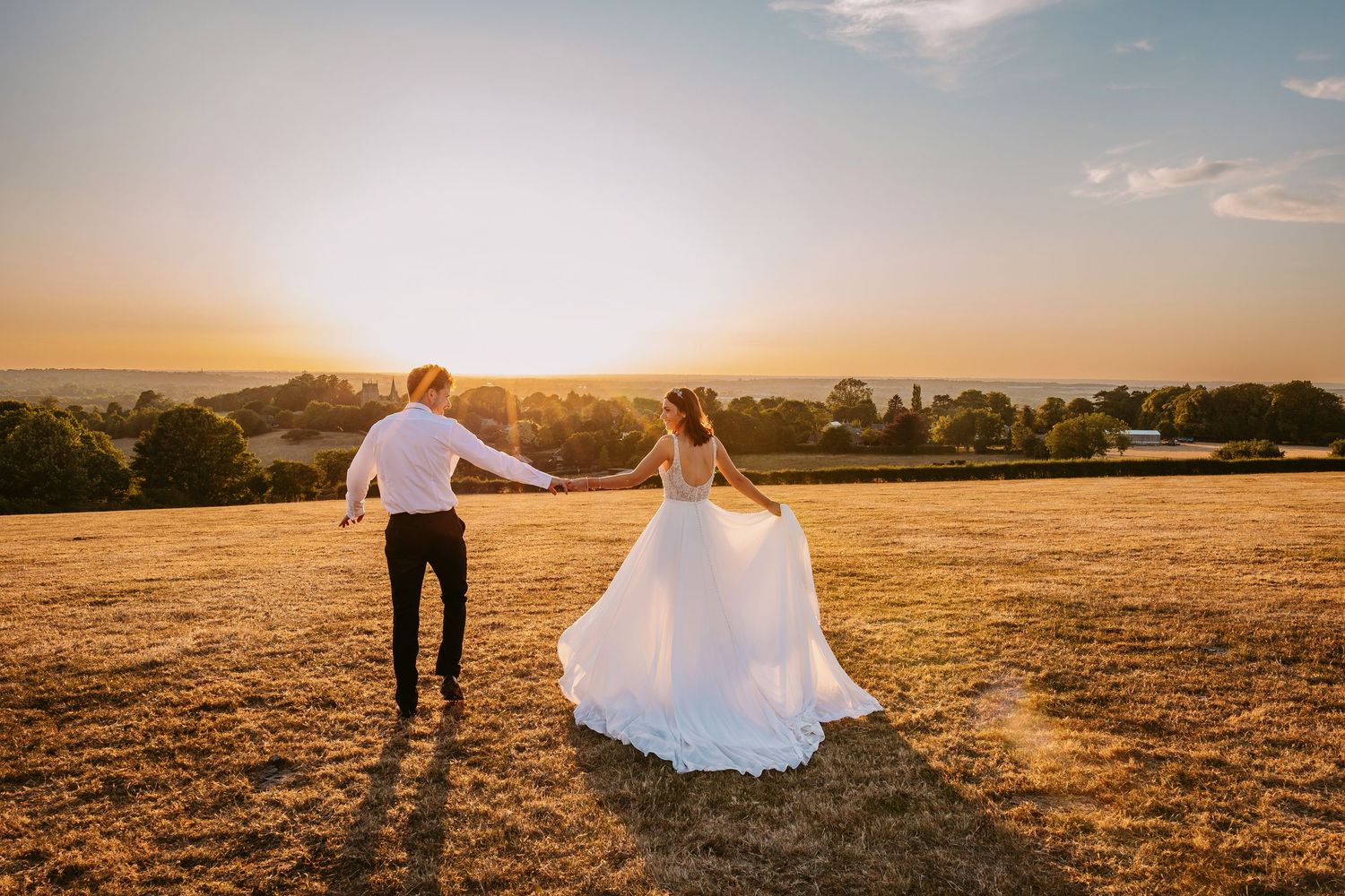 Wedding couple walks through a sun-drenched field with dramatic lighting at golden hour.