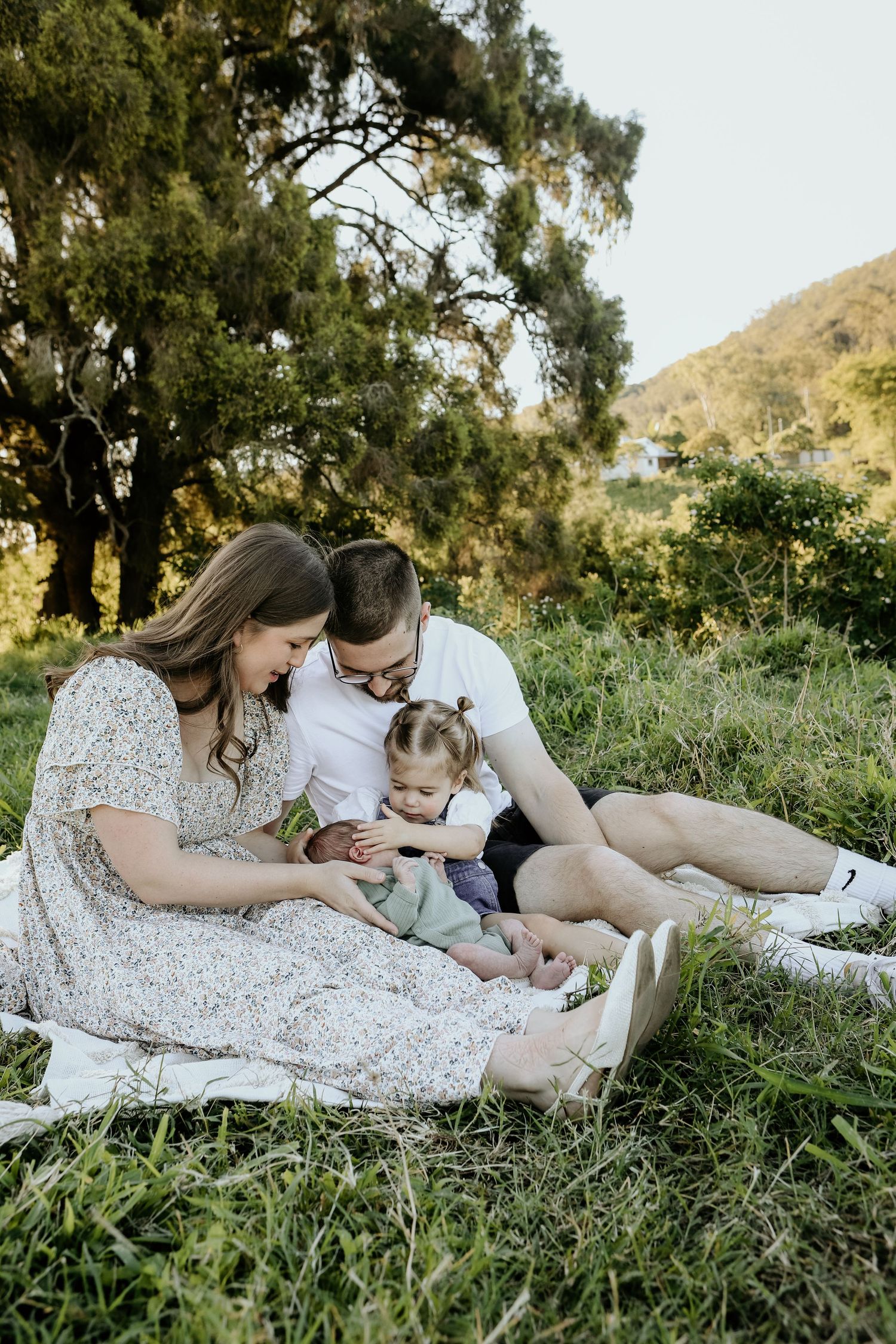 Family relaxing together on grassy hillside during golden hour in nature.