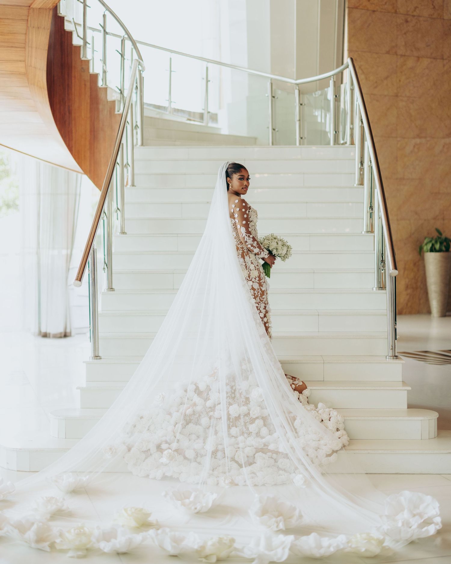 A stunning white wedding dress with floral embellishments cascades down an elegant staircase in natural light.