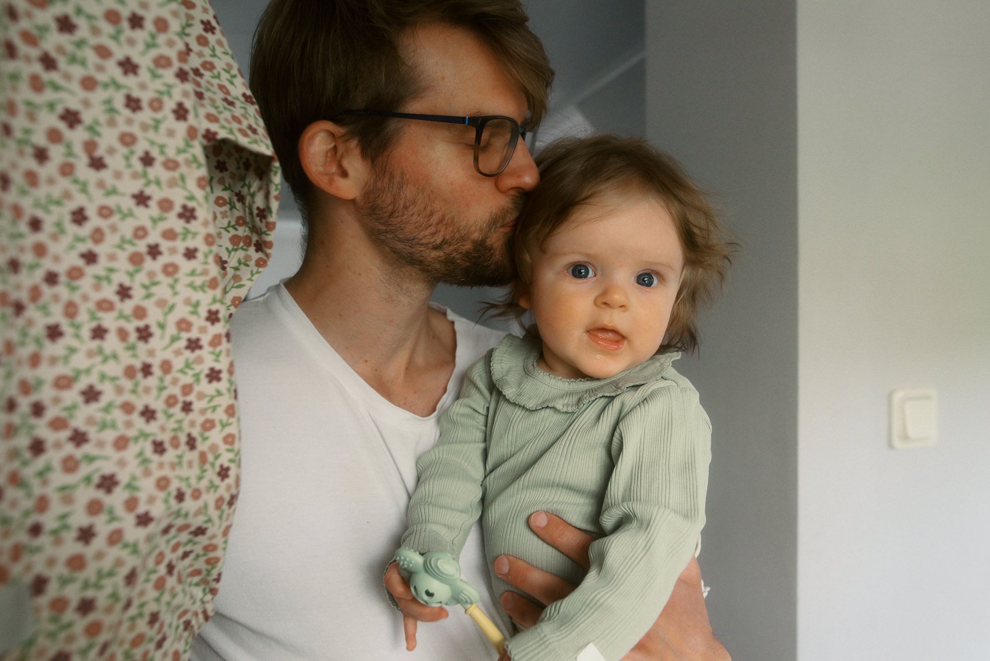 Parent and child share tender moments together against neutral backdrop with floral wallpaper accent.