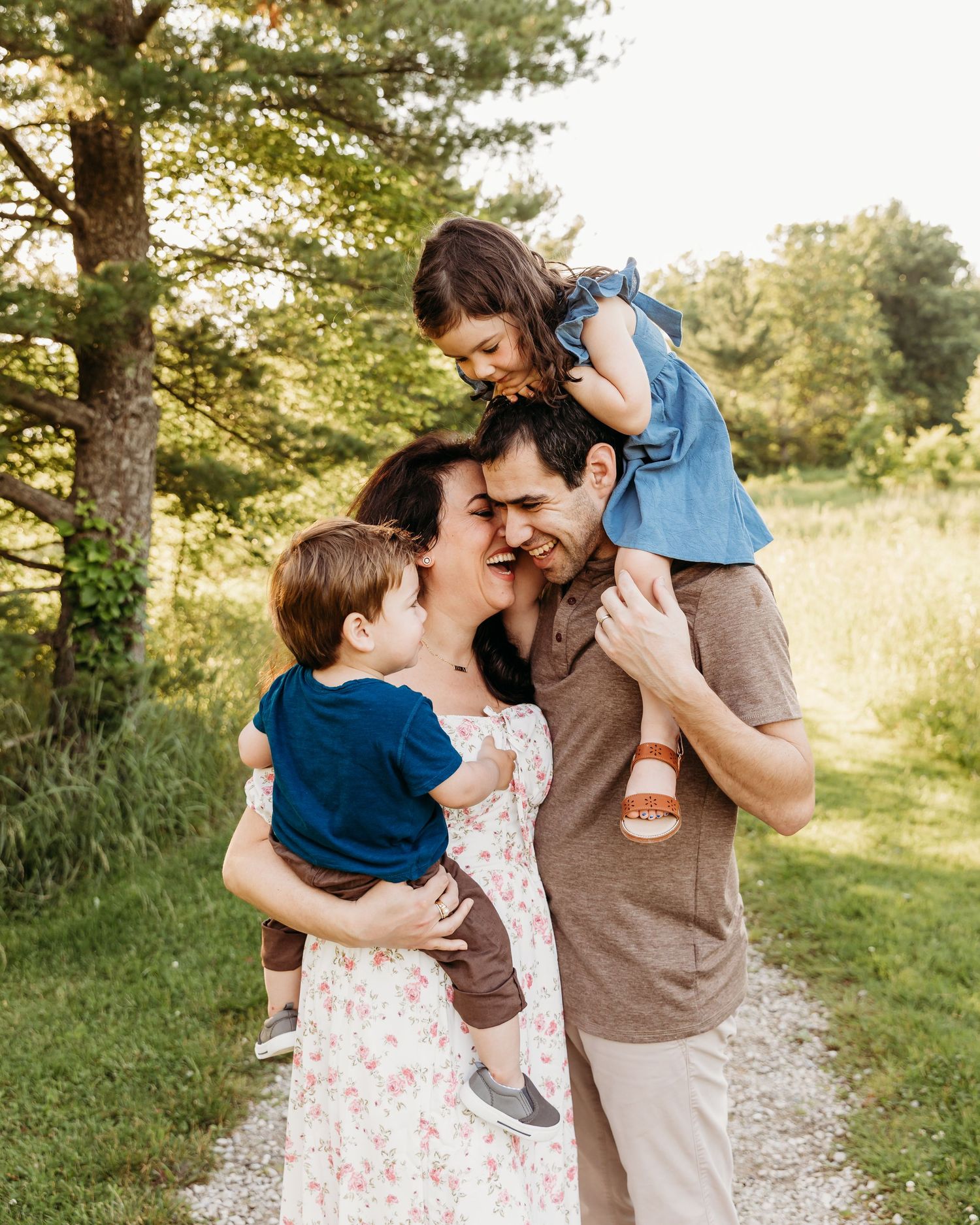 Cleveland Family Photographer- A family shares tender moments together on a sunlit path surrounded by pine trees and tall grass.