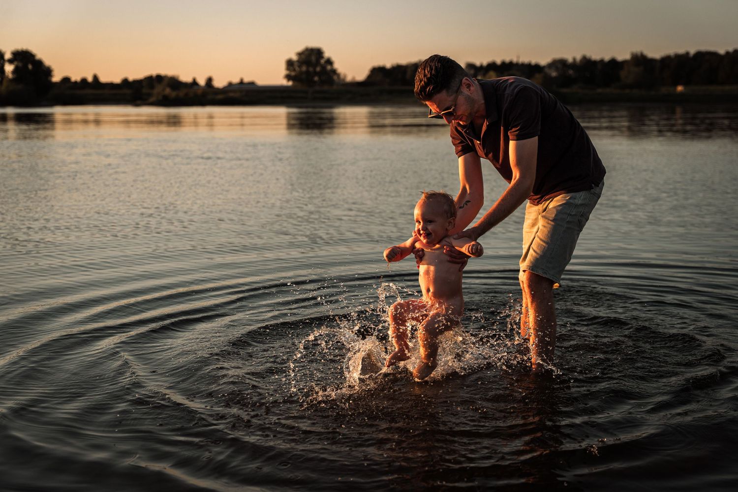 People splash and play in a lake during sunset creating ripples in the water.