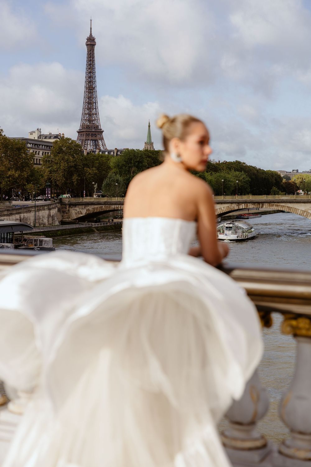 Flowing white wedding dress captured on a Parisian bridge with the Eiffel Tower in the distance. Paris, France