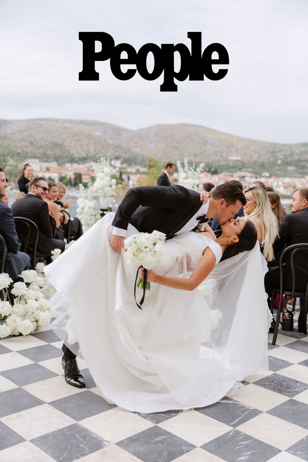 Romantic wedding couple performs dramatic dip pose on black and white checkered floor with mountain backdrop. People Magazine, Adam Huber