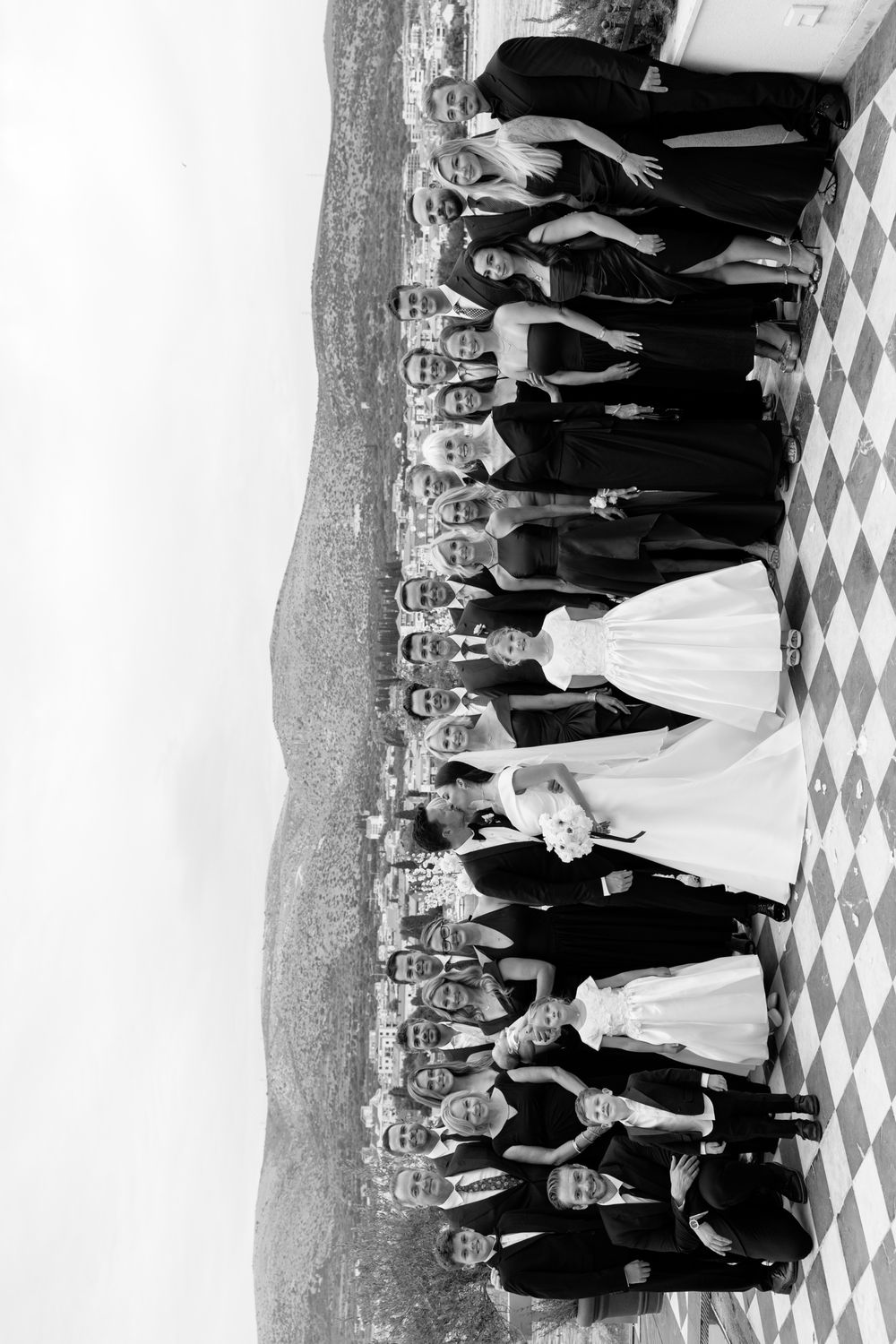 A formal black and white wedding party poses together on a checkered floor at an elegant venue.