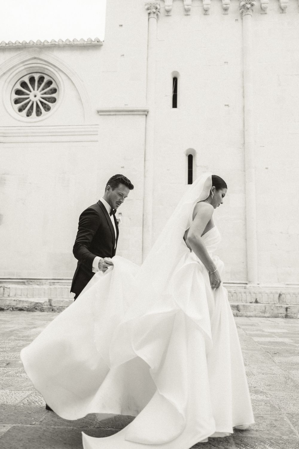 A series of black and white wedding photos showing a flowing white dress against architectural details of a church exterior, Adam Huber