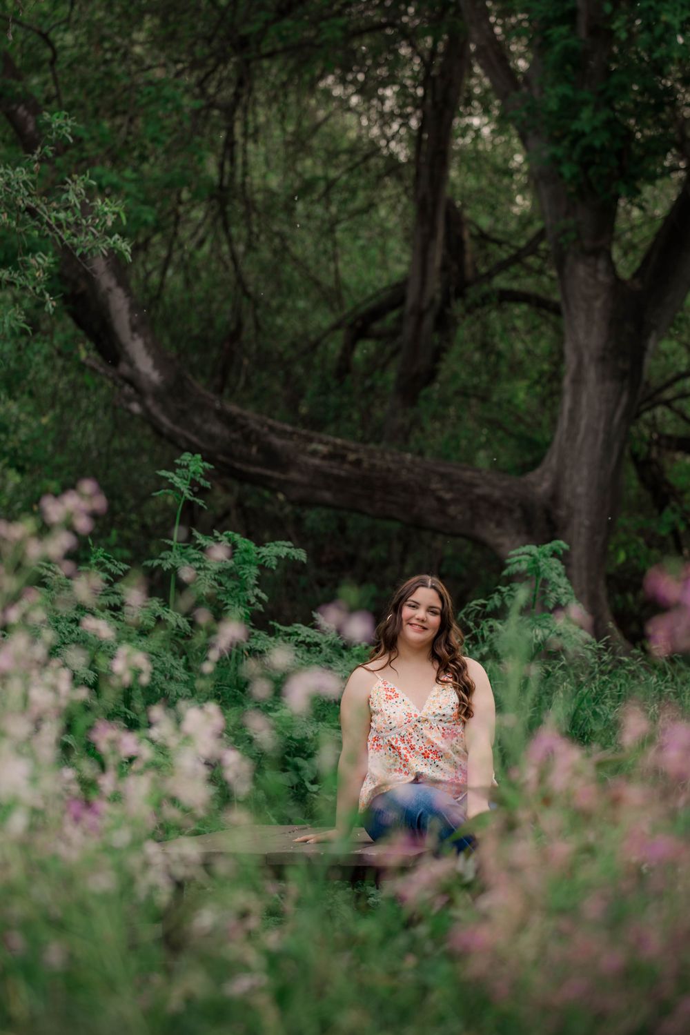 A pink floral dress stands out against lush green foliage in a wooded outdoor setting.
