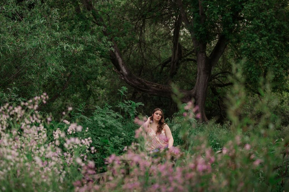 A couple walks through a lush green forest pathway with pink wildflowers blooming along the trail.