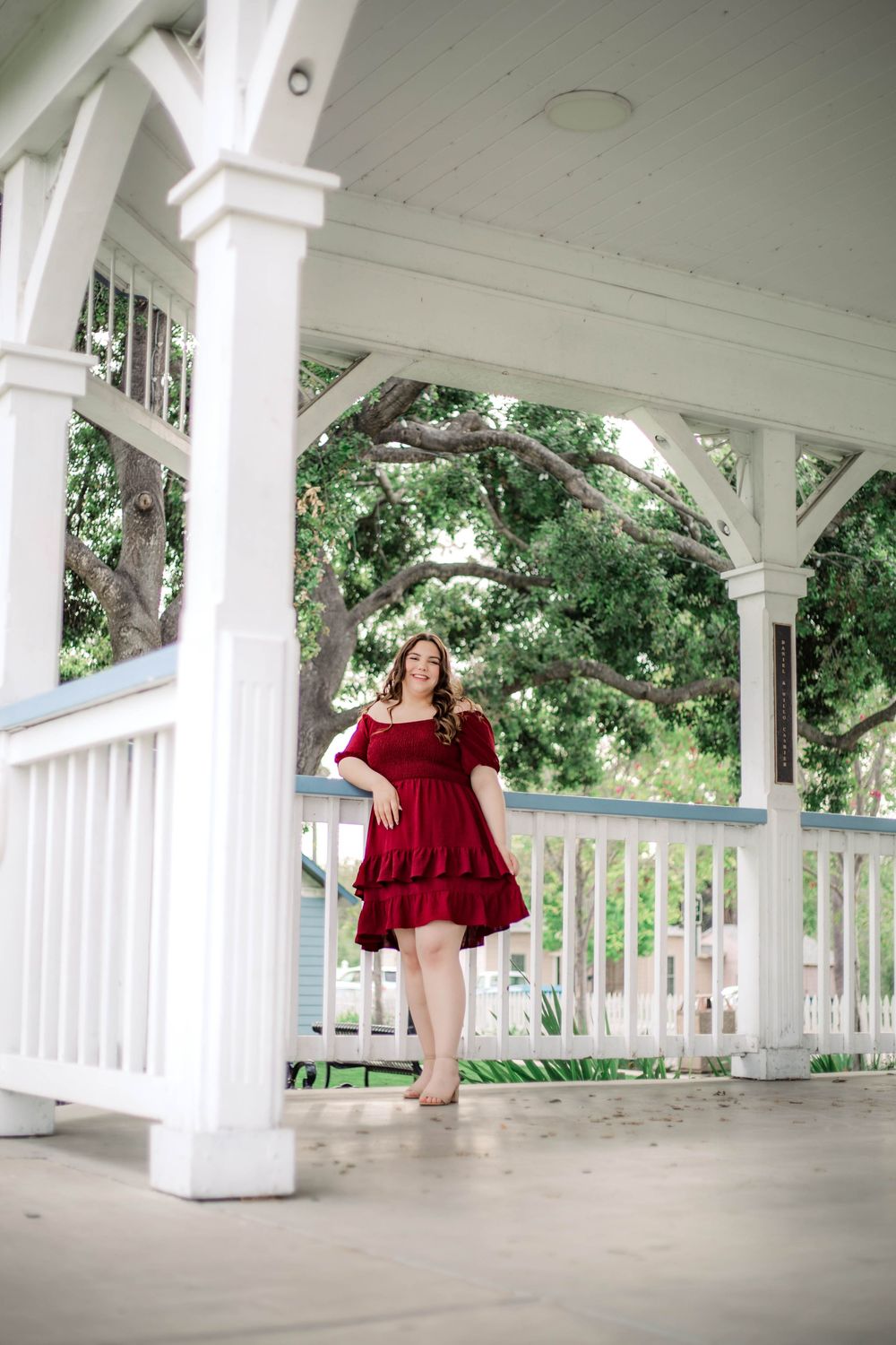 A red dress creates elegant contrast against white pillars of a covered porch.