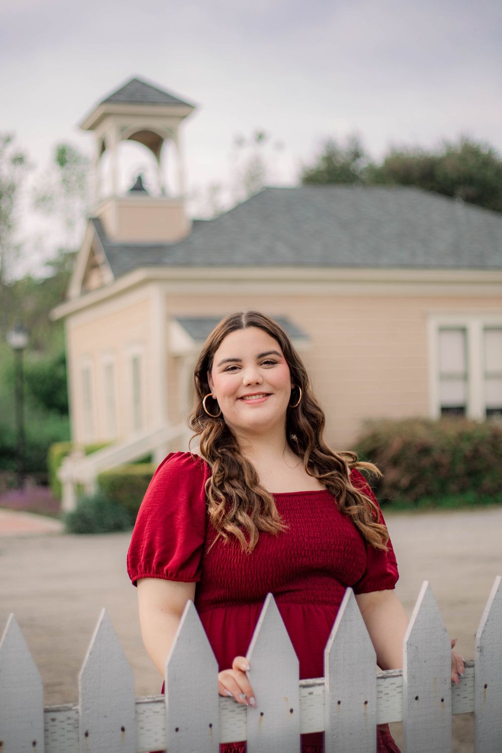A red dress provides a pop of color against a white picket fence and beige building.