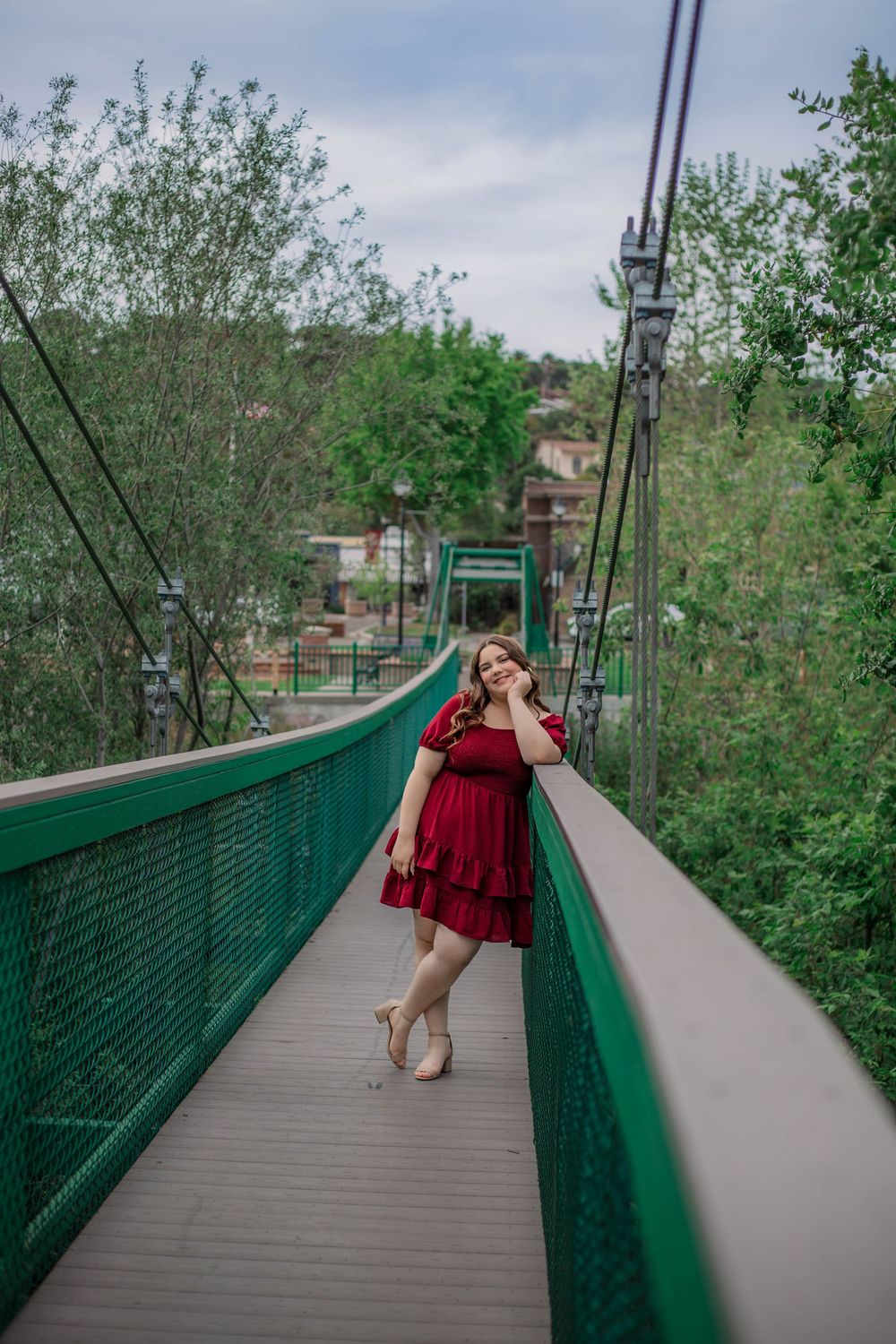 Four sequential photos of a person in a red dress walking along a green-railed pedestrian bridge pathway.