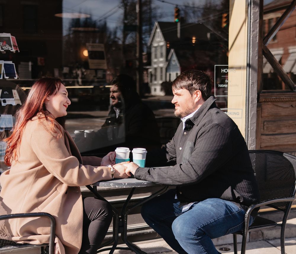 Two people sit at an outdoor cafe table having coffee together on a chilly day.
